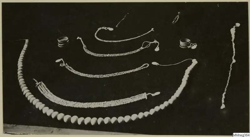 Necklaces, rings and bracelets of pale beads laid out on a dark background