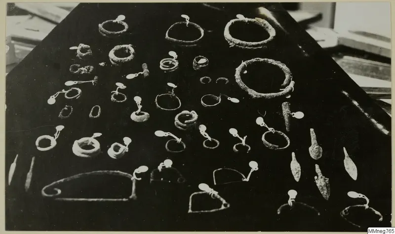 Corroded metal rings, pins and arrowheads laid out in rows on a black cloth