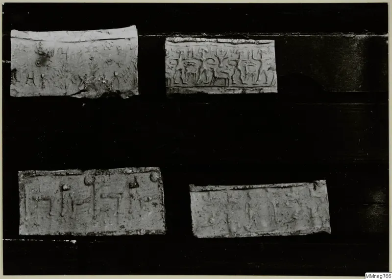 Four pale rectangular pieces with impressed designs of figures and signs, laid on a dark background.