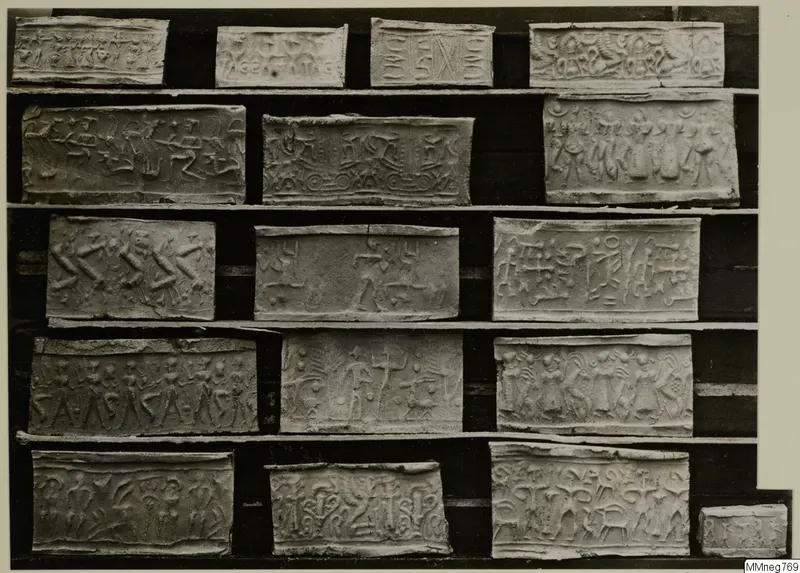 Rows of pale rectangular seal impressions with carved figures and animals, arranged on a dark board.