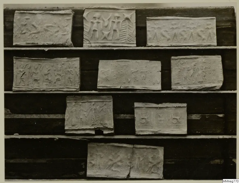 Ten pale rectangular impressions with stamped designs of figures and signs, arranged on wooden shelves