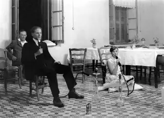 Two people smoking narghilés in a tiled room in Kyrenia, with a third man seated in the doorway behind them