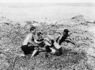 Four bathers play on a seaweed-covered rocky shore by the sea at Kyrenia.