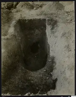 Tomb 302 at Lapithos during excavation, with a dark oval opening at the base of a deep rectangular cut in the soil