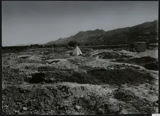 Excavation at Lapithos with mounds of earth and a white tent, with mountains behind.
