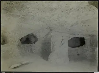 Interior of rock-cut Tomb 313 A at Lapithos, with a central rock pillar and two dark side recesses in the walls.