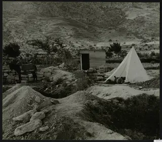Excavation at Lapithos with a white tent, a wooden hut and a donkey beside a stone wall