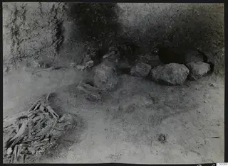 Tomb 303 a at Lapithos during excavation, with a jumbled skeleton in the lower left and large stones along the chamber wall.