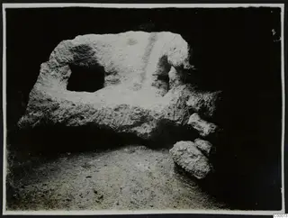 Tomb 306 at Lapithos during excavation, showing the tomb chamber wall with a square opening and stones at the right.