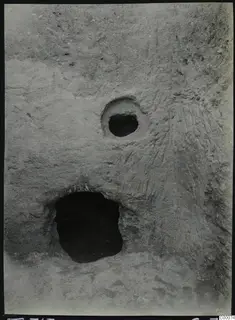 Tomb 313 at Lapithos during excavation: dark tomb opening and a small round hole in a cut face of pale soil