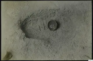 Tomb 322 at Lapithos during excavation, with a small vessel holding pale round objects in the sandy floor.