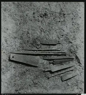 Corroded metal objects, including blades and pins, lying in soil during excavation of Tomb 322 at Lapithos