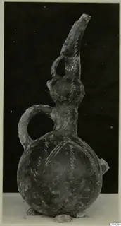 Pottery jug with a tall spout-like neck, two handles and pale hatched lines on its body, photographed against a dark background