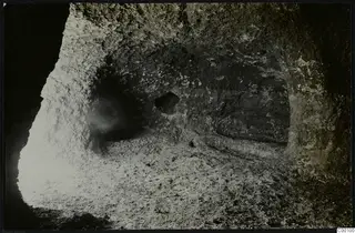 Interior of rock-cut Tomb 322 b at Lapithos, with a rough rock-cut chamber wall and a loose stony floor