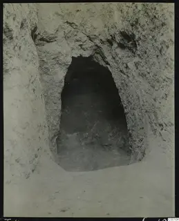 Tomb 409 at Lapithos: arched entrance opening into a dark tomb chamber cut into pale earth