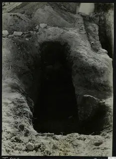 Tomb 416 at Lapithos Kastros during excavation, showing a rectangular opening in the ground with stones inside the dark chamber.