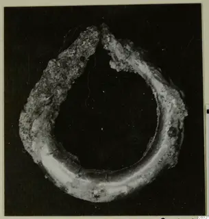 Bronze earring, an open hoop with a corroded, crusted surface, photographed against a dark background.