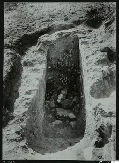 Tomb 403 at Lapithos Kastros during excavation, with stones lying in the dark fill of the tomb chamber.