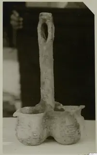 Pottery vessel with two deep rounded bowls joined at the base and a tall flat handle with an oval hole at the top