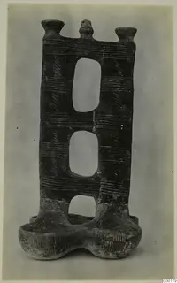 Dark pottery vessel with three oval openings, two cup-like rims at the top and a two-lobed base, from Lapithos