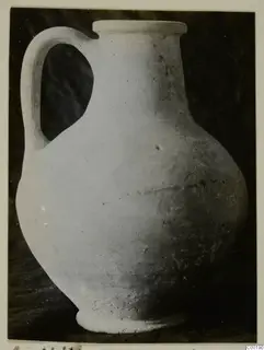 Plain white jug with a strap handle and a flat-topped rim, photographed against a dark background.