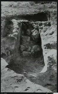 Tomb 401 at Lapithos Kastros during excavation, with large stones lying in the cut chamber among the soil.