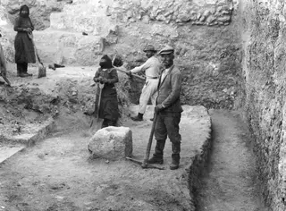 Excavation at Soli: workers with shovels and a pick in a trench beside stone walls and steps
