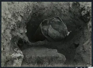 Broken pottery vessel lying in an excavated pit at Soli, with a large stone block at the edge of the cut.