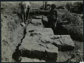 Excavation at Soli with workers, shovels and a wheelbarrow beside exposed large stone blocks in a trench