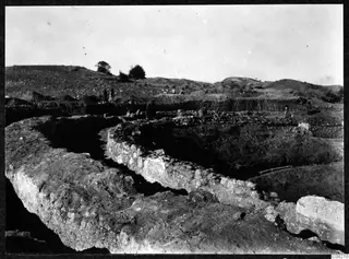 Excavated stone walls of the theatre at Soli in the foreground, with workers on the spoil-covered ground behind.