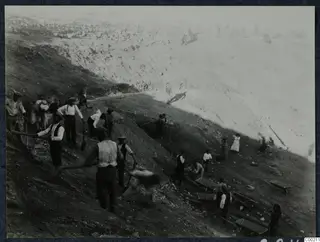 Excavation at the theatre at Soli, with workers digging a steep slope and carrying stones away in wheelbarrows.
