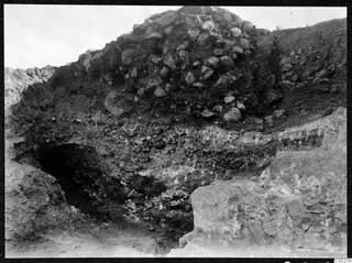 Excavation trench at Soli with a heap of stones above dark soil layers and a pale rock face at right