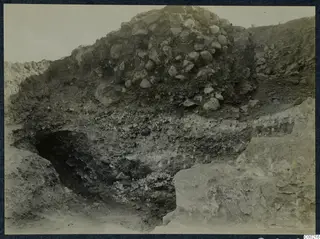 Excavation at the theatre at Soli, with a mound of stones above layers of soil and a pale cut rock face at right.