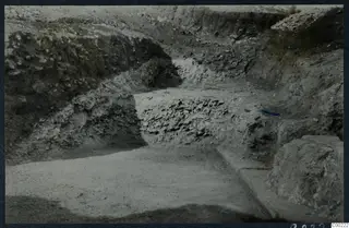 Excavation trench at the theatre at Soli, with exposed stones in the banks and a worked stone block at the right edge