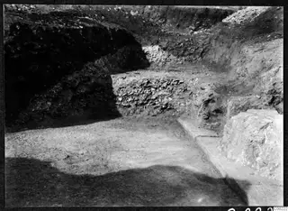 Excavation trench at the Soli theatre with a bank of loose stones, a large pale stone block and a long stone edge