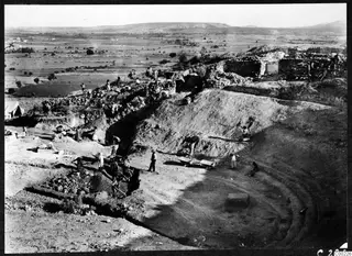 Excavation of the orchestra of the theatre at Soli, seen from the west, with workers, wheelbarrows and a stone wall above.