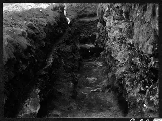 Excavation trench at Soli with exposed stone walling on the right and layered soil on the left.