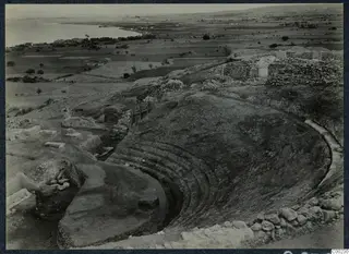 Excavated theatre at Soli with curved tiers of seating cut into the slope, with the sea and plain beyond.