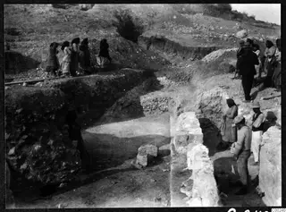 Excavation at the theatre at Soli, with people standing at the trench edges beside cut stone blocks and a rubble wall.