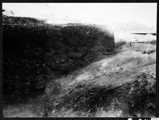 Excavation trench at Soli with a dark soil section on the left and a pale, stony rock surface on the right.