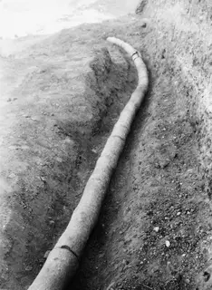 Long clay pipe lying in a narrow excavated trench at Soli, curving away into the distance.