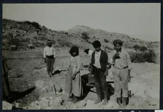 Woman and young men standing among rough stones on a dry hillside at Soli, with a cart behind them