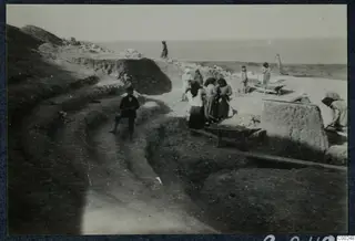 Excavation at Soli theatre with workers, a wheelbarrow and cut stone blocks, the sea on the horizon