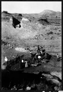 Excavation at the theatre at Soli, with workers digging and pushing wheelbarrows in a trench below cut walls on a hillside
