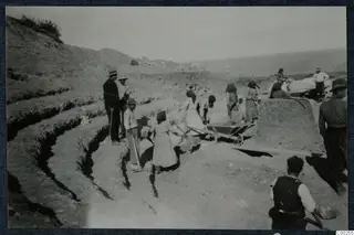 Excavation at Soli theatre with workers, a wheelbarrow and stepped cuttings in the ground, sea in the distance