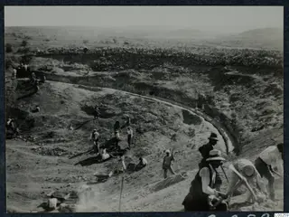 Excavation of the curved theatre at Soli, with workers digging with picks and wheeling soil in a wheelbarrow.