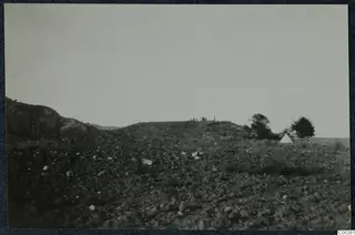 Stony hillside at Soli with a few small figures on the ridge top and a white tent beside a tree