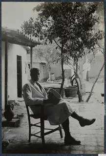 Alfred Westholm seated on a wooden chair in a courtyard, holding a wide bowl in his lap