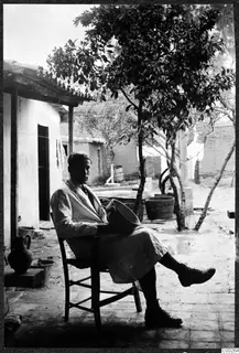 Alfred Westholm seated on a wooden chair in a courtyard, holding a wide vessel on his lap.