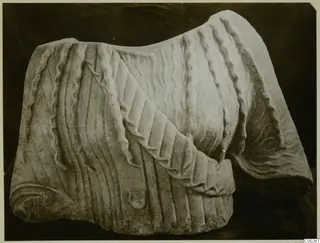 Marble sculpture fragment from Galini showing pleated drapery over the shoulder and wavy hair, seen from the front.